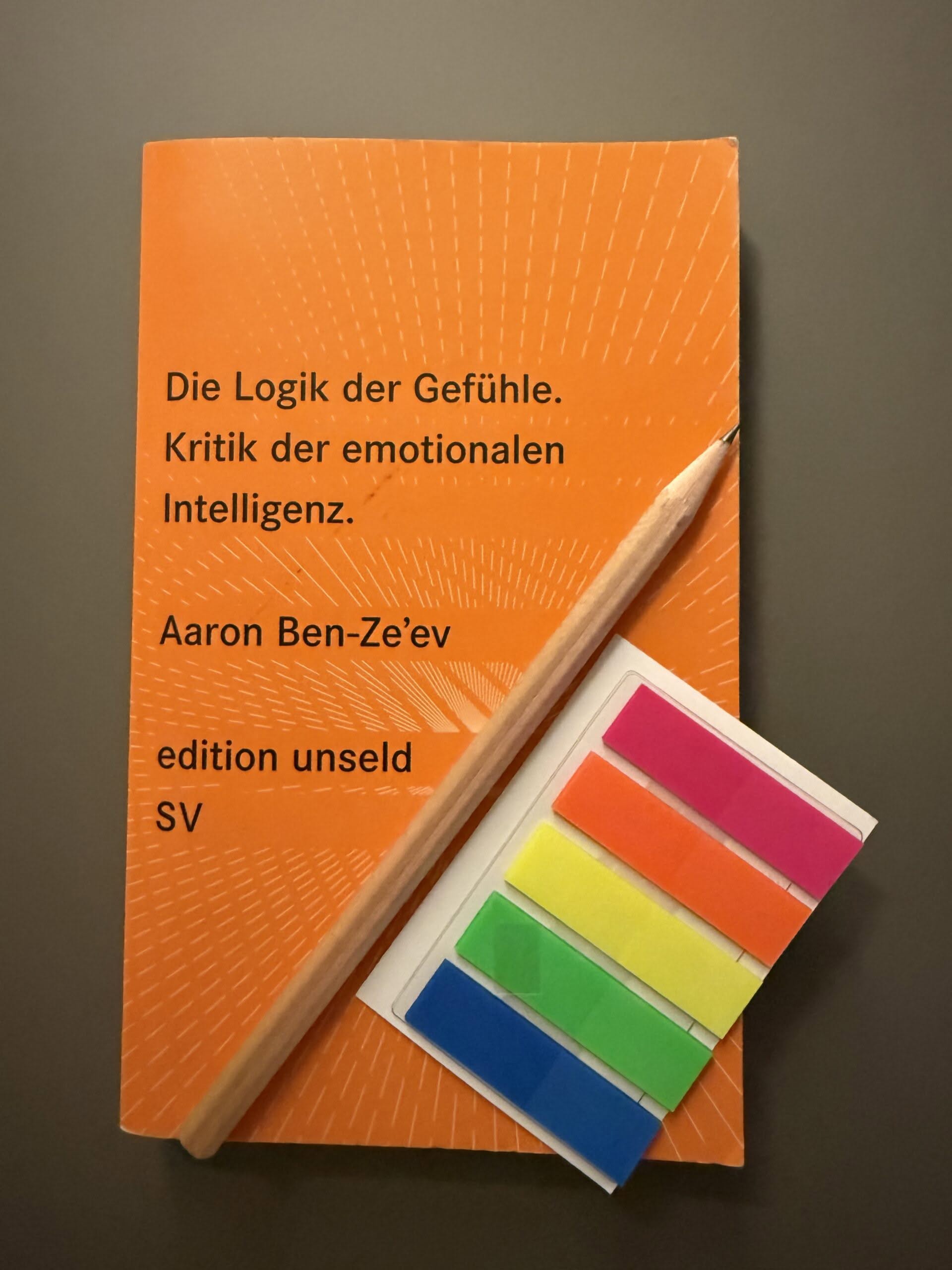 Das Buch "Ben-Ze'ev, Aaron (2009): Die Logik der Gefühle. Kritik der emotionalen Intelligenz" auf grauem Untergrund. Rechts neben dem Buch liegen ein Bleistift und ein Briefchen bunter Markierungsklebestreifen.